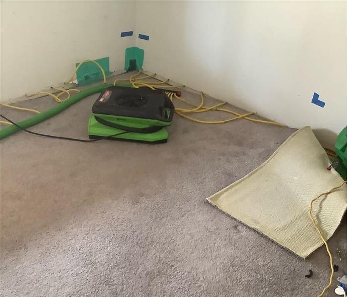 room affected by water being dried out by air movers and injecto dry, small yellow tubes providing air floor into the wall 