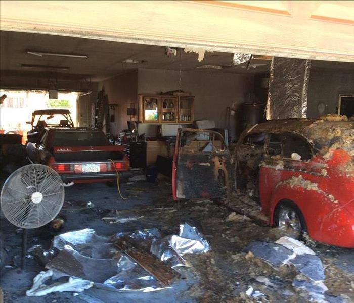 Residential garage fire with fallen drywall and insulation on top of a classic car. Black visible smoke damage throughout