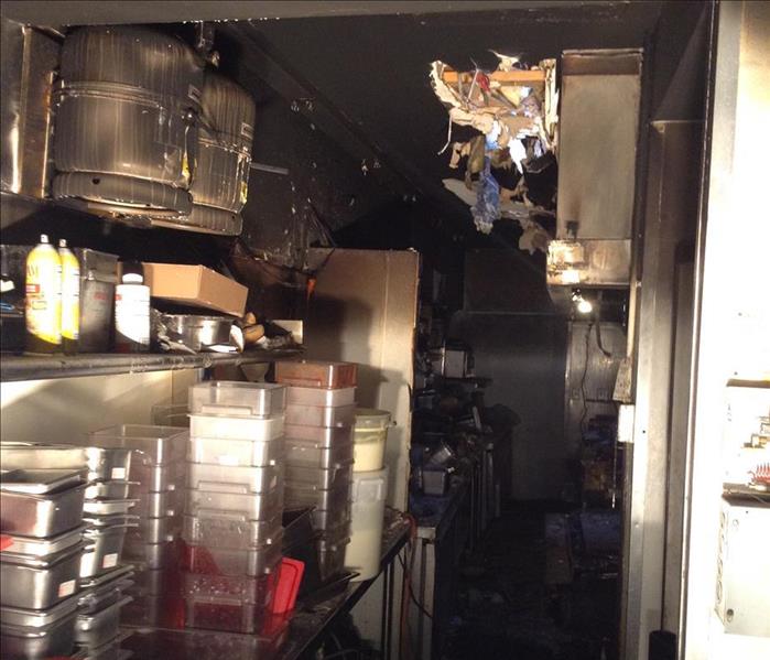The aftermath of a fire in a commercial kitchen.  Black smoke visible throughout the kitchen 